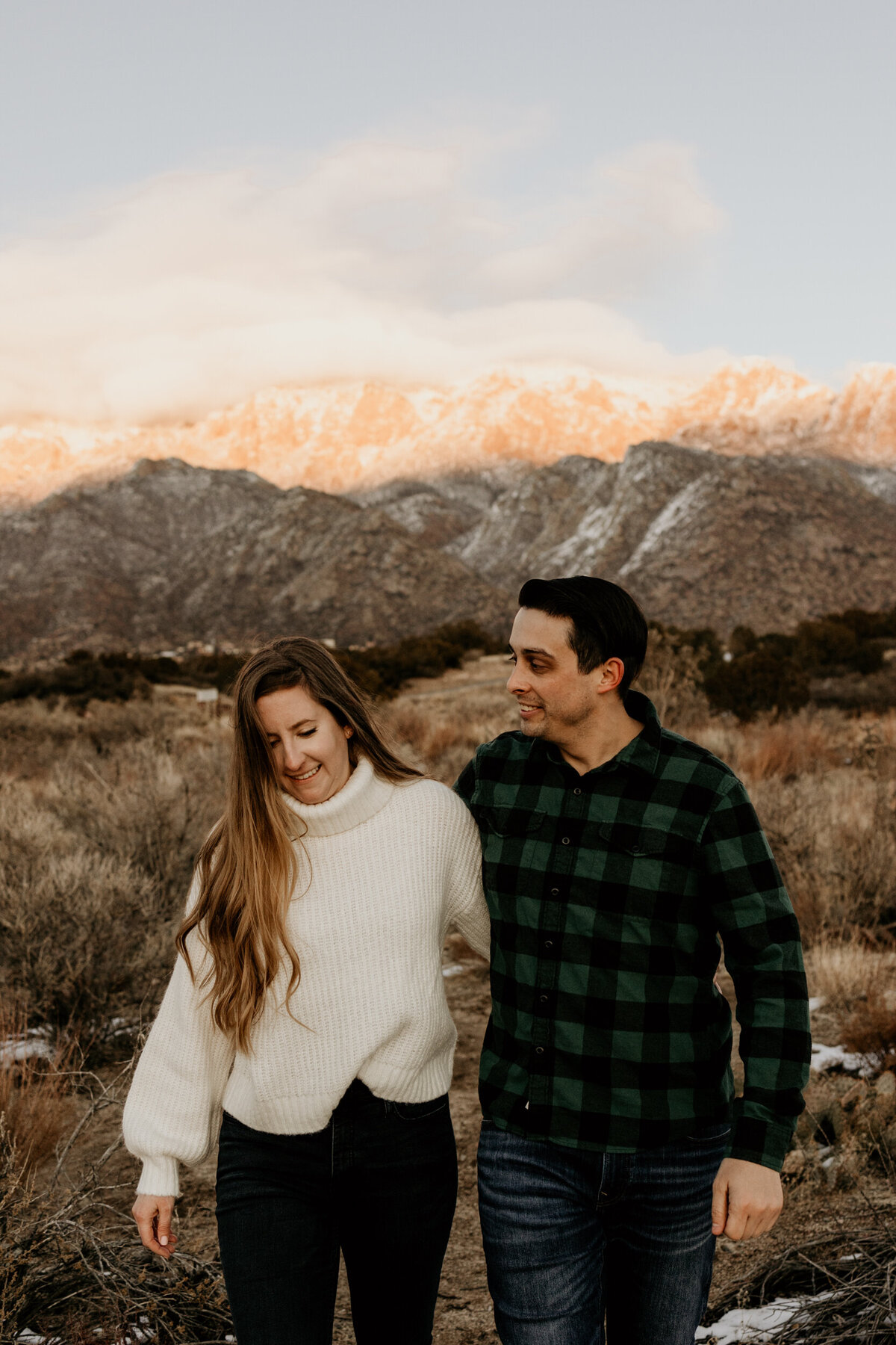 engaged couple walking in the New Mexico desert with a snowy mountain behind them