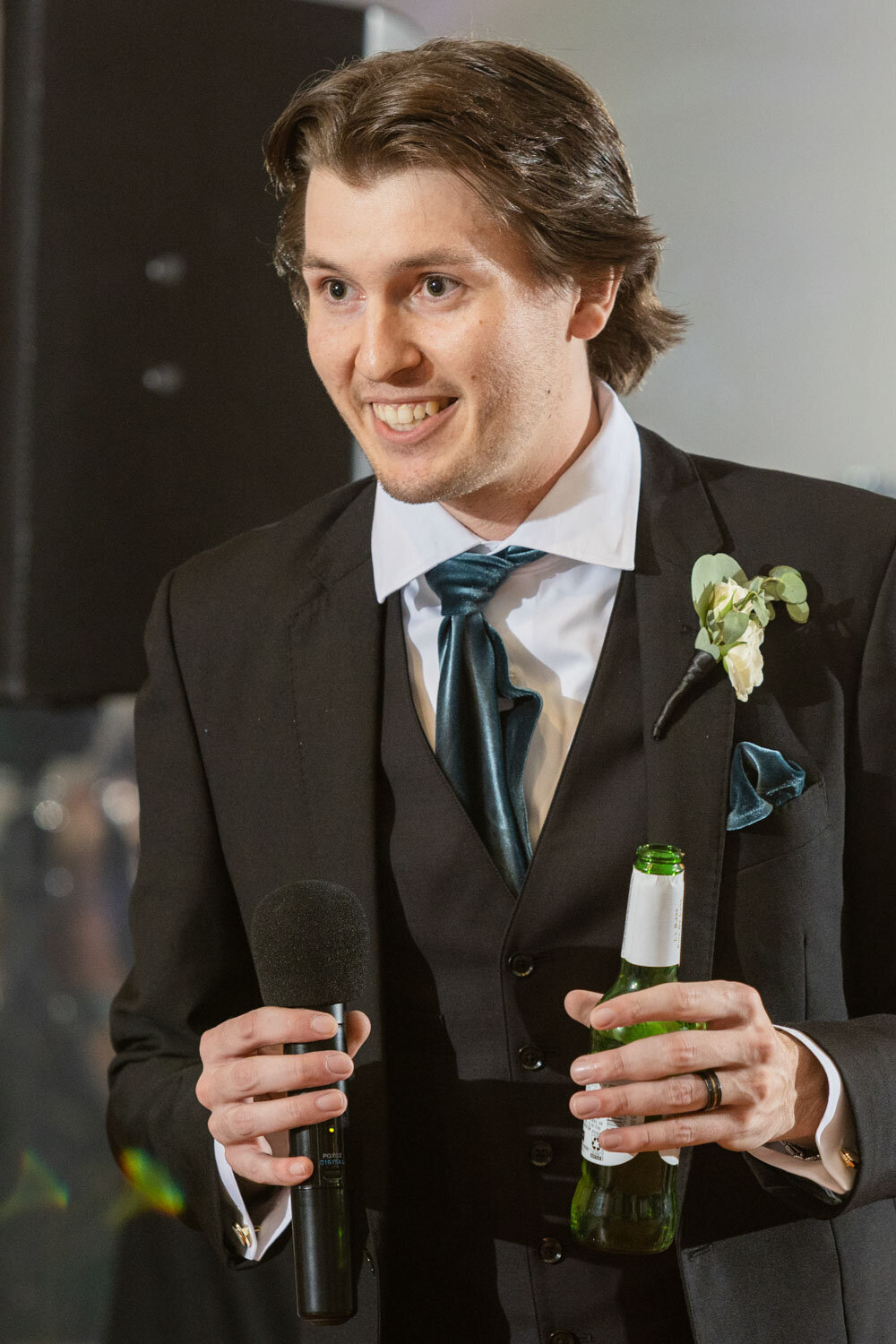 A man in a suit and tie is holding a microphone and a bottle of beer