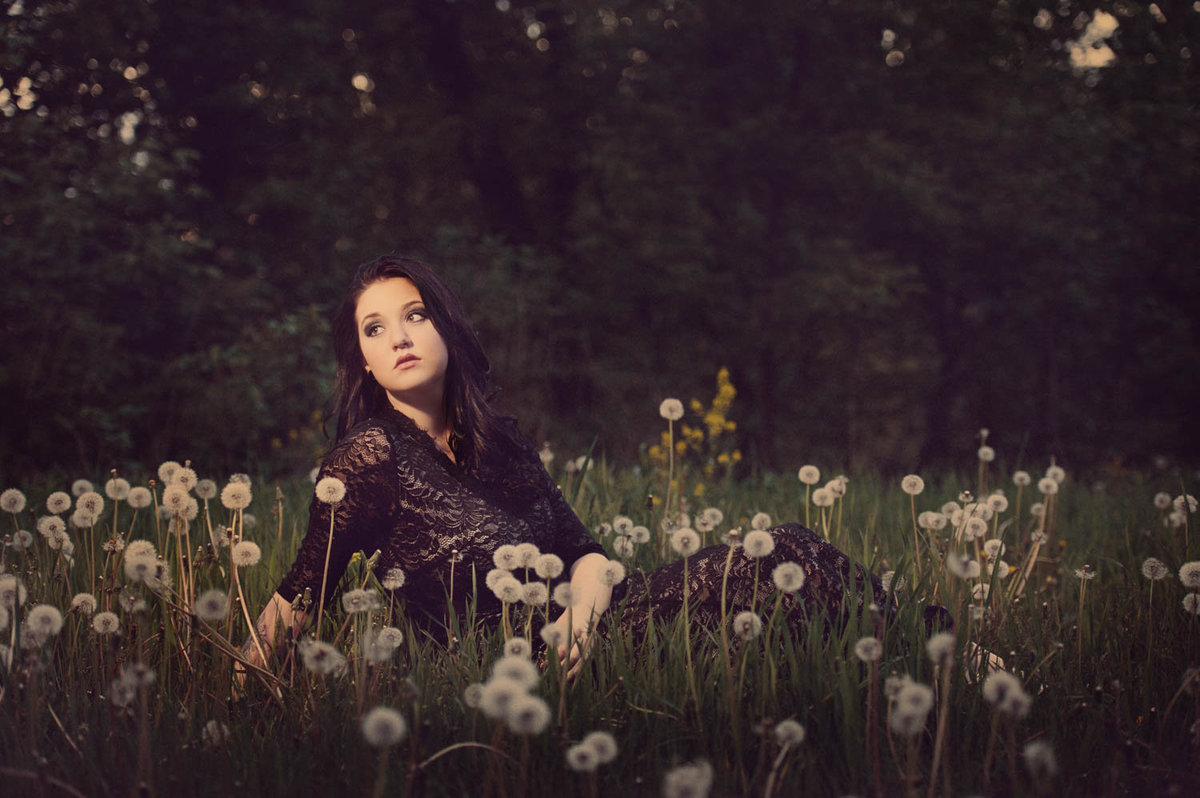 girl in black lace fashion dress sitting in field of dandelions