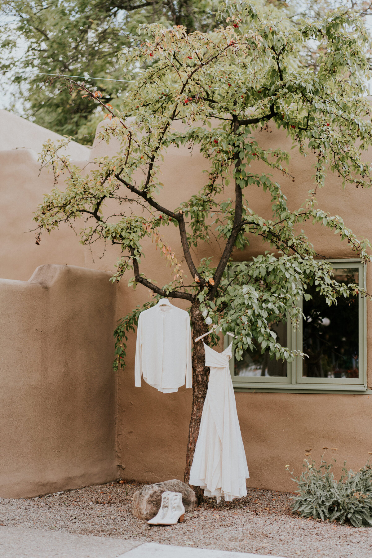 Wedding dress hung from a tree with white boots and a white jacket.