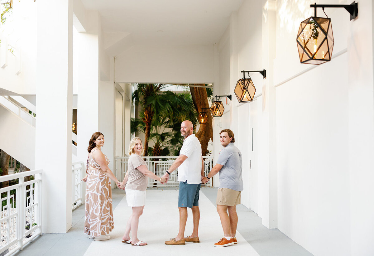 Elegant family portrait in a modern outdoor corridor, holding hands and smiling for the camera. Florida Keys family sessions with Claudia Amalia Photography.