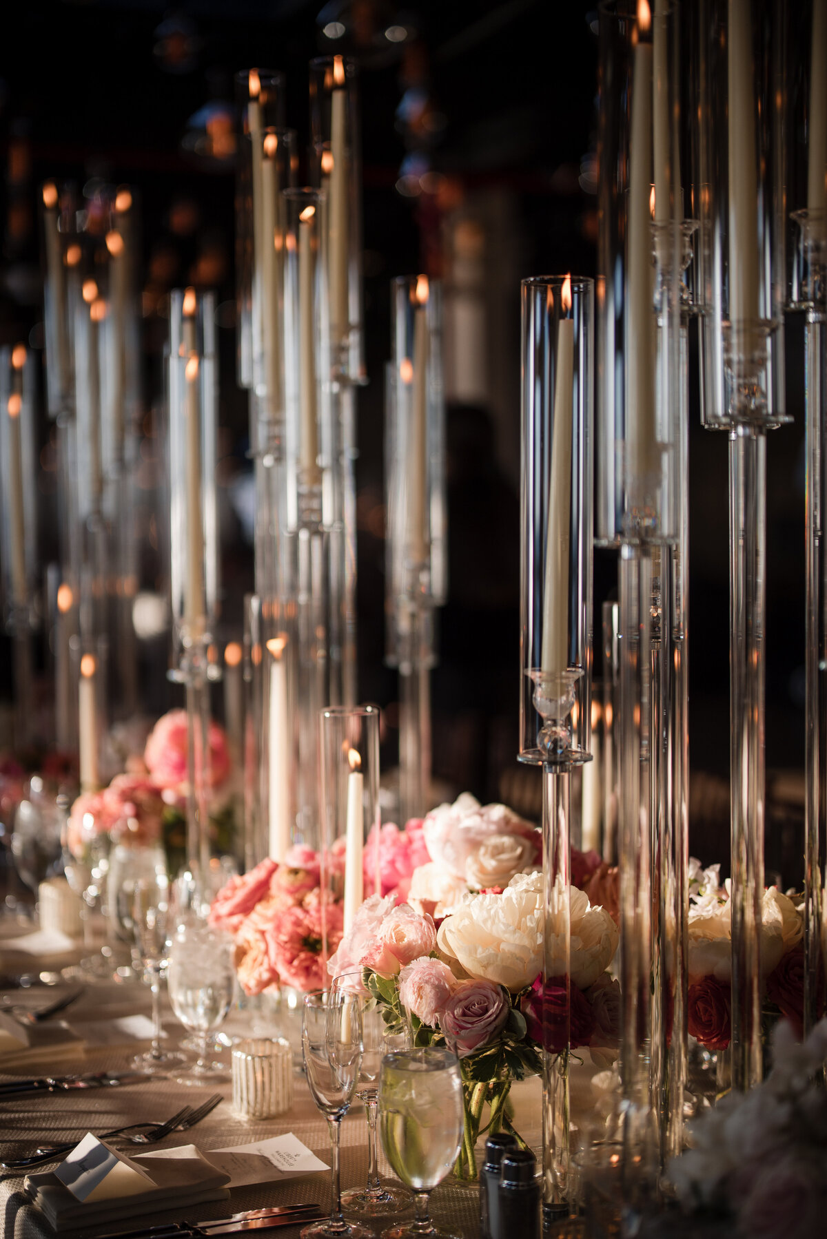 Elegant table setting with tall candlesticks, pink and white floral arrangements, and neatly arranged tableware. This photo was taken by a NYC wedding photographer