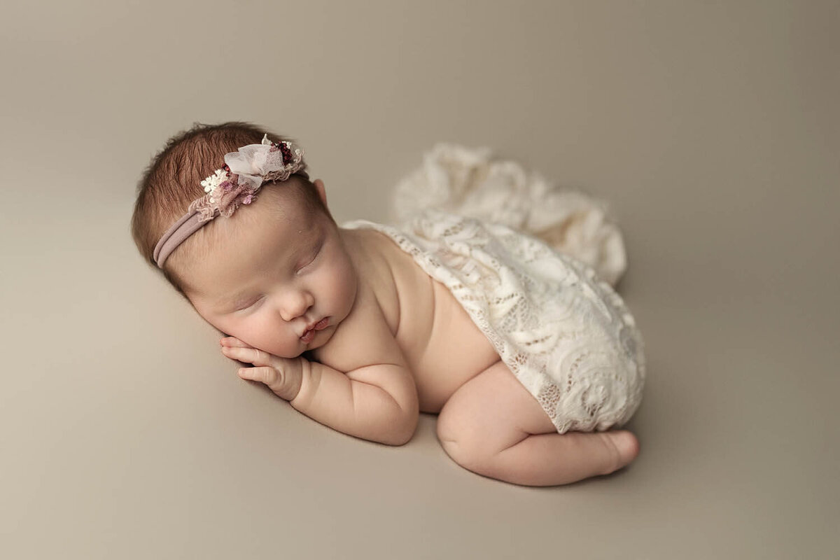 A sleeping newborn baby wrapped in a lace blanket in a studio