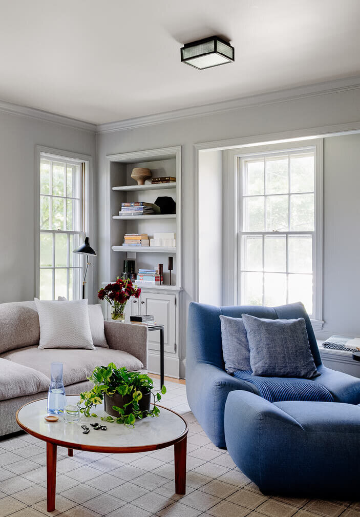 Modern and simple family room with a bold blue chair in a historic Hingham home, designed by a South Shore interior decorator, blending style and history.