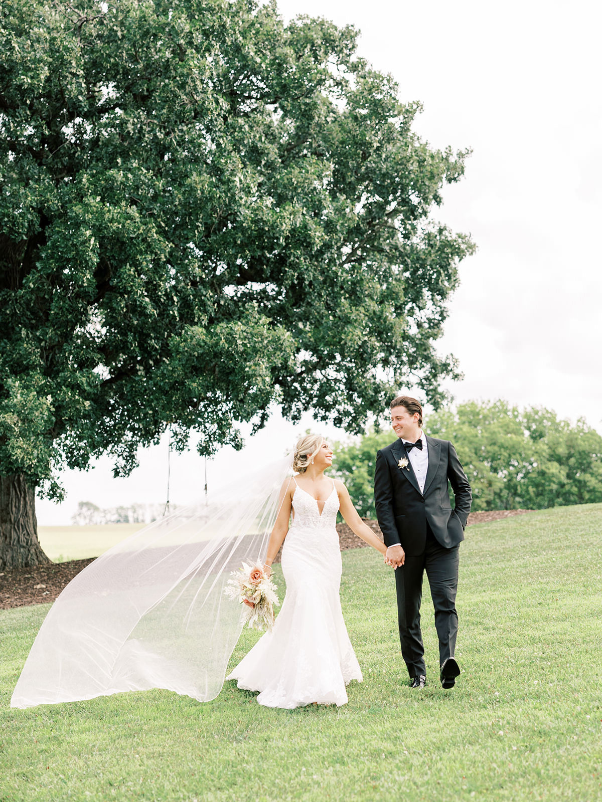 Bride and groom hold hands and walk across expansive field while veil blows in the wind