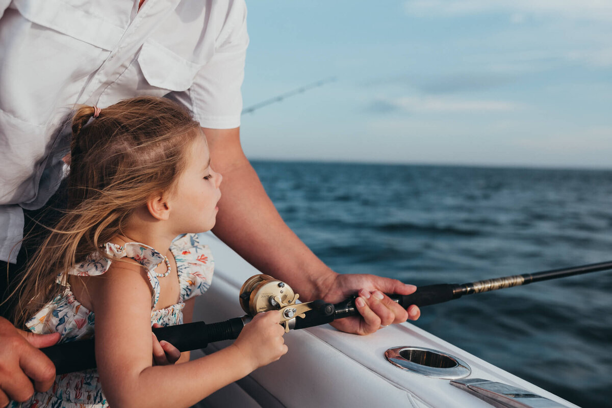 A father helps his young daughter hold one of his deep sea fishing rods on their family boat