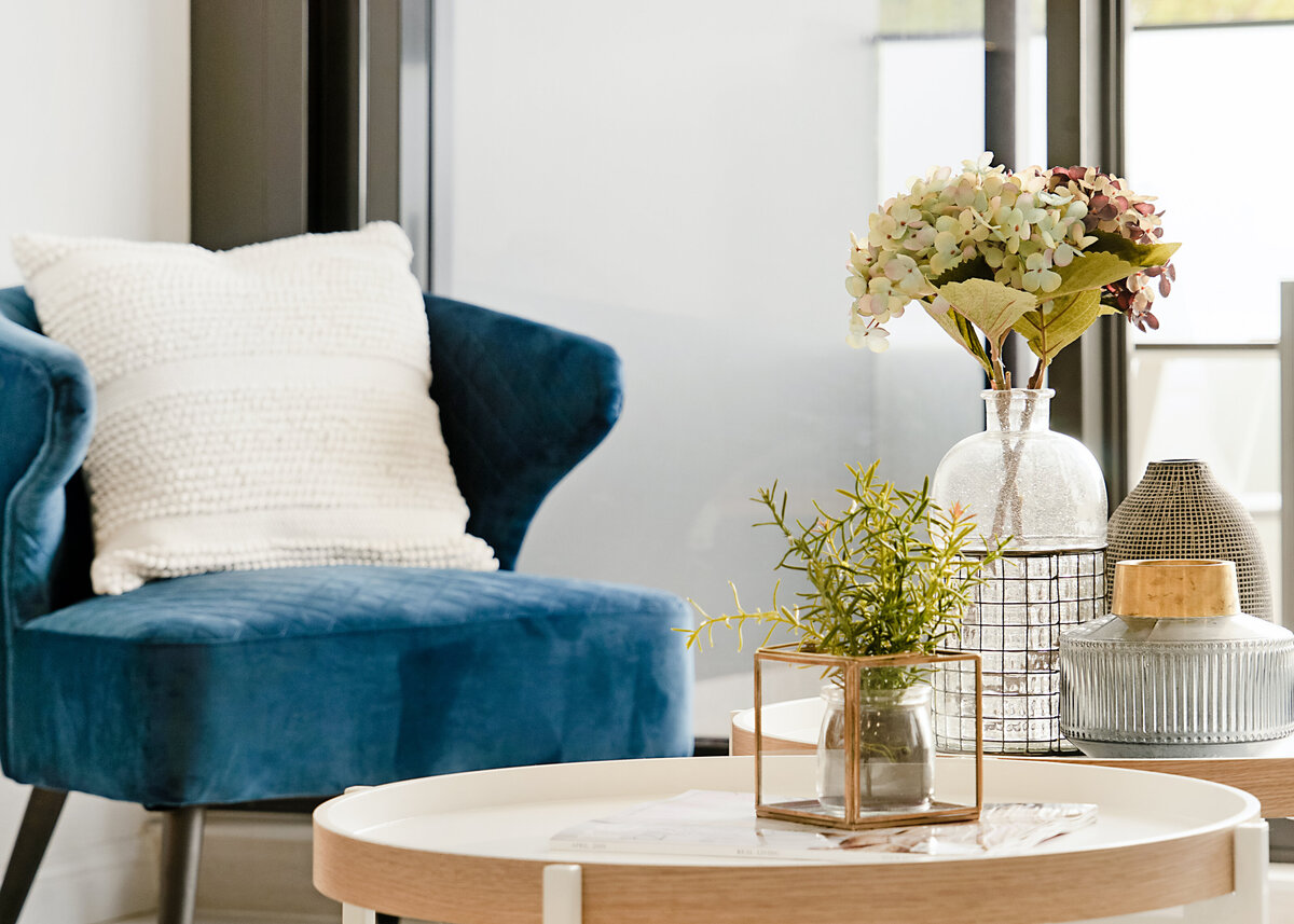 A blue velvet chair is styled with vases and hydrangeas on a wooden coffee table in this interior design.