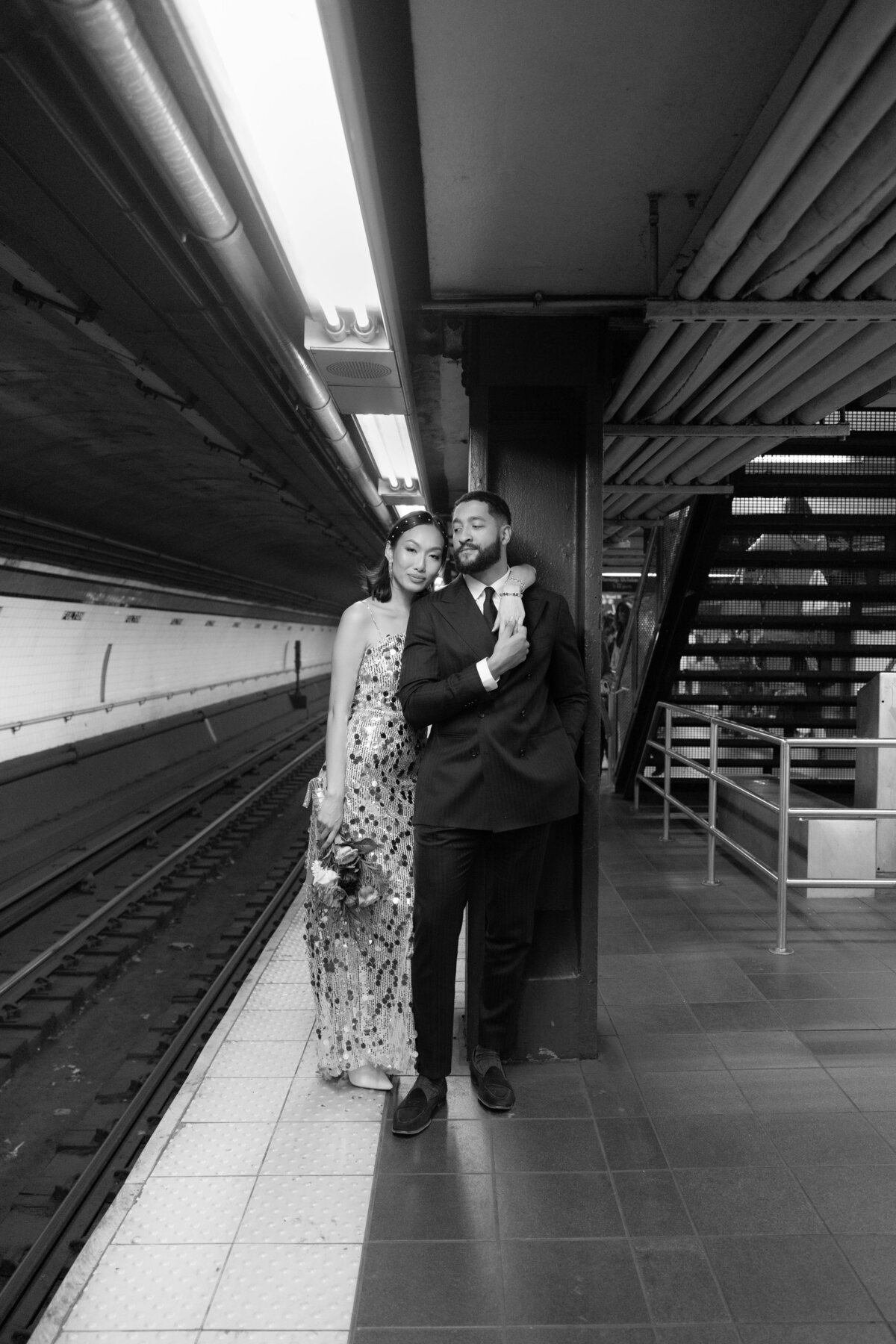 The couple shares a playful laugh on the subway platform, surrounded by the urban energy of New York City.