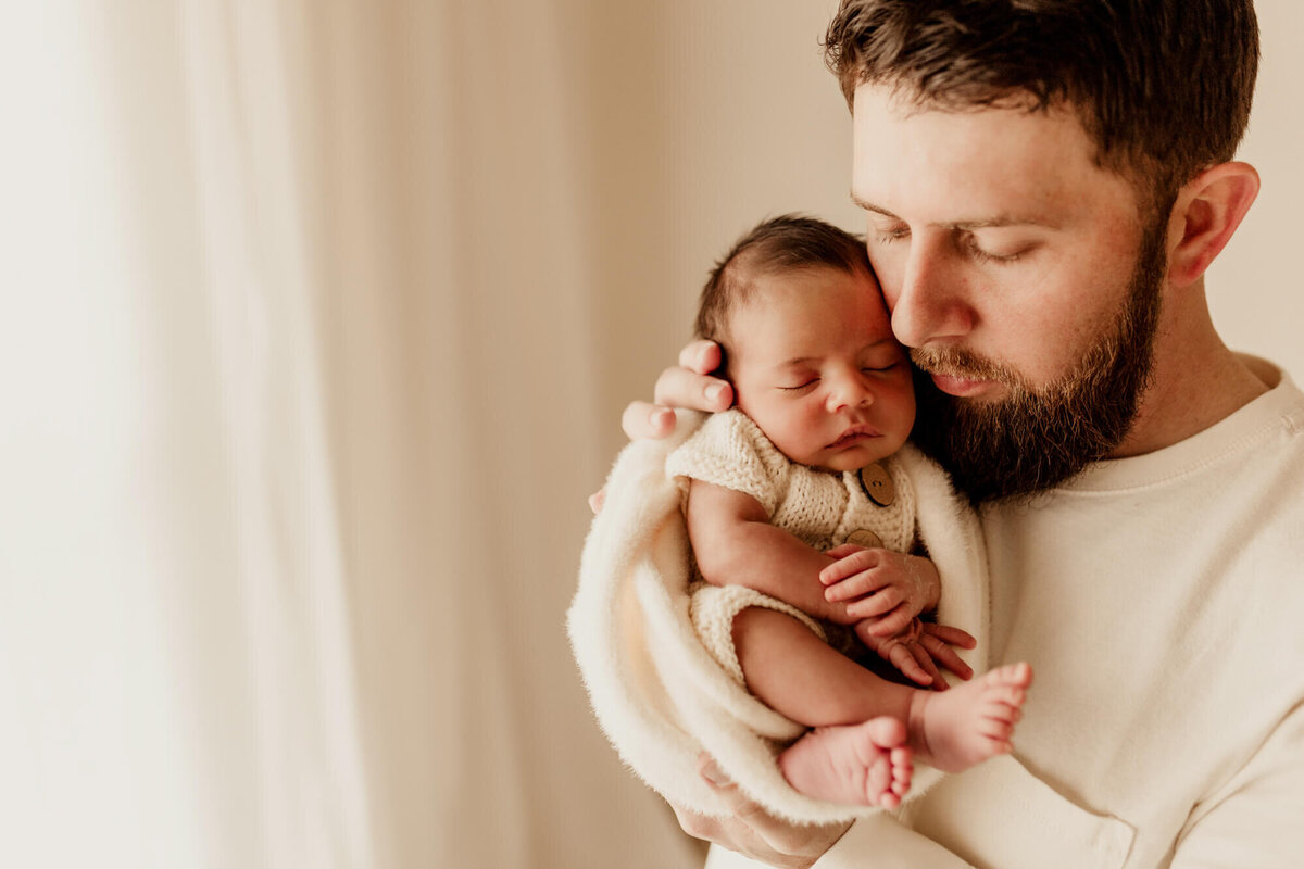Father holds his son next to his cheek as he sleeps.