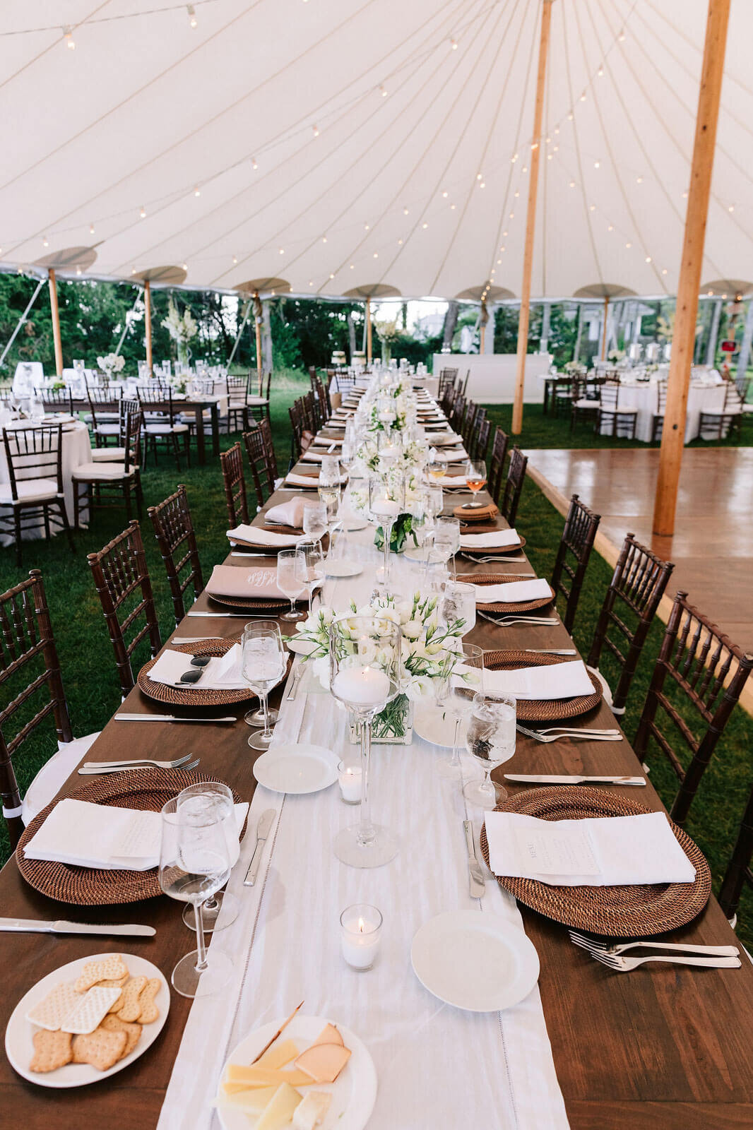 A long wood dining table, with a white table runner and white flower centerpieces and cutleries in Cape Cod Summer Tent, MA