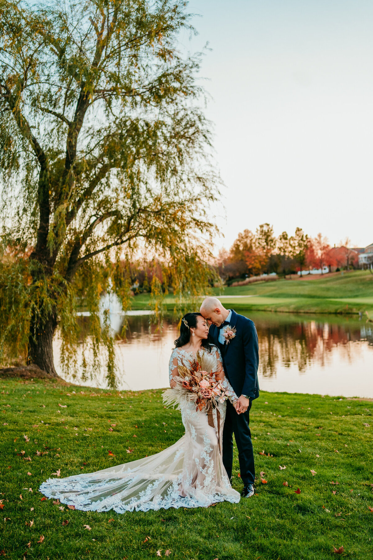 Couple kissing near a pond under a willow tree at sunset