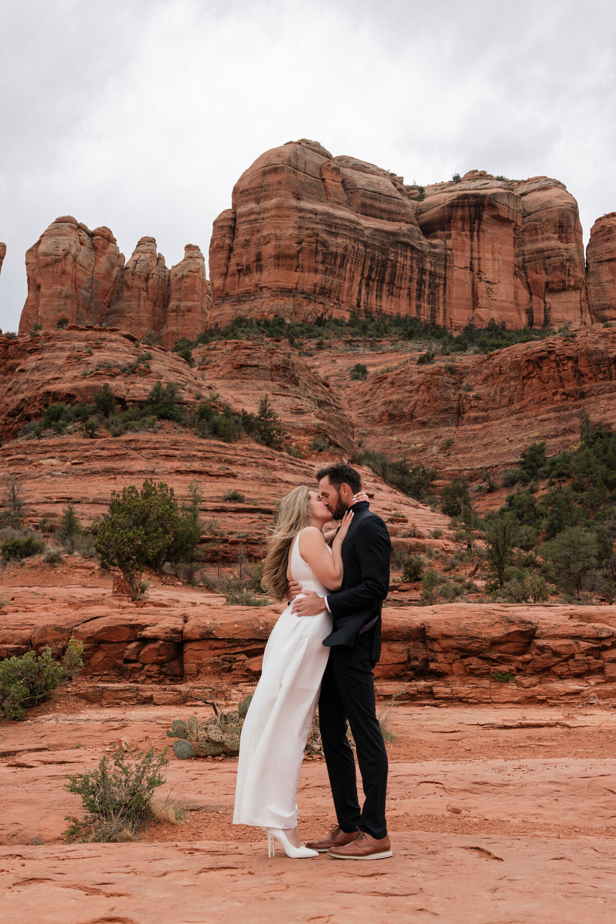 Bride and groom share a romantic kiss during their elopement at Cathedral Rock in Sedona, Arizona, surrounded by iconic red rock cliffs and desert landscape.