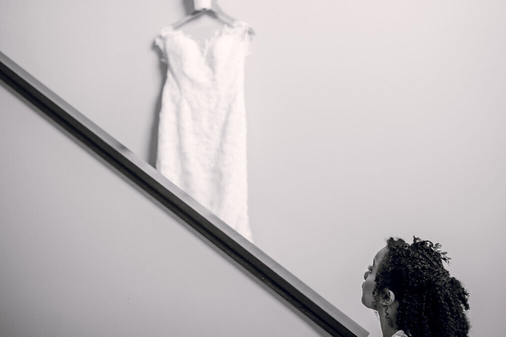 A bride looking at her wedding dress hanging on the stairs.