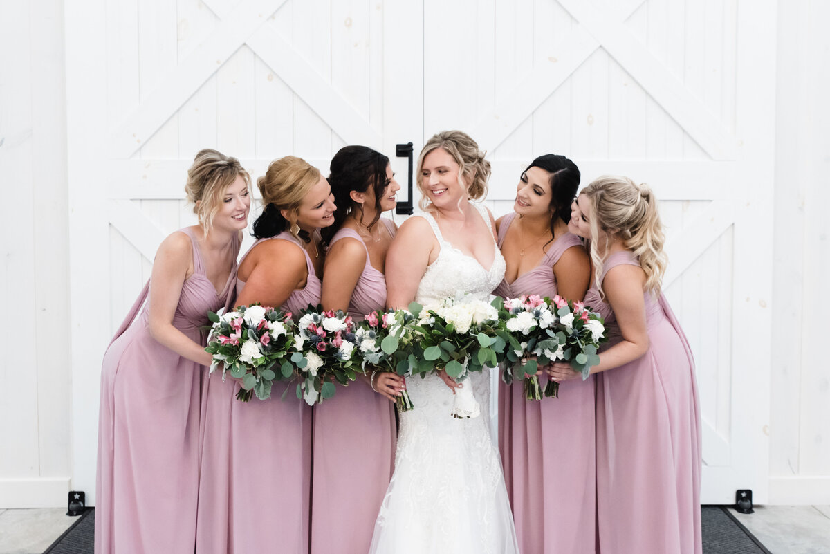 bride with bridesmaid in pink smile at each other inside barn at grayson house