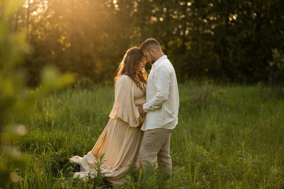 Pregnant woman wearing a beige Reclamation Dress hugging her husband in a field in Ottawa.