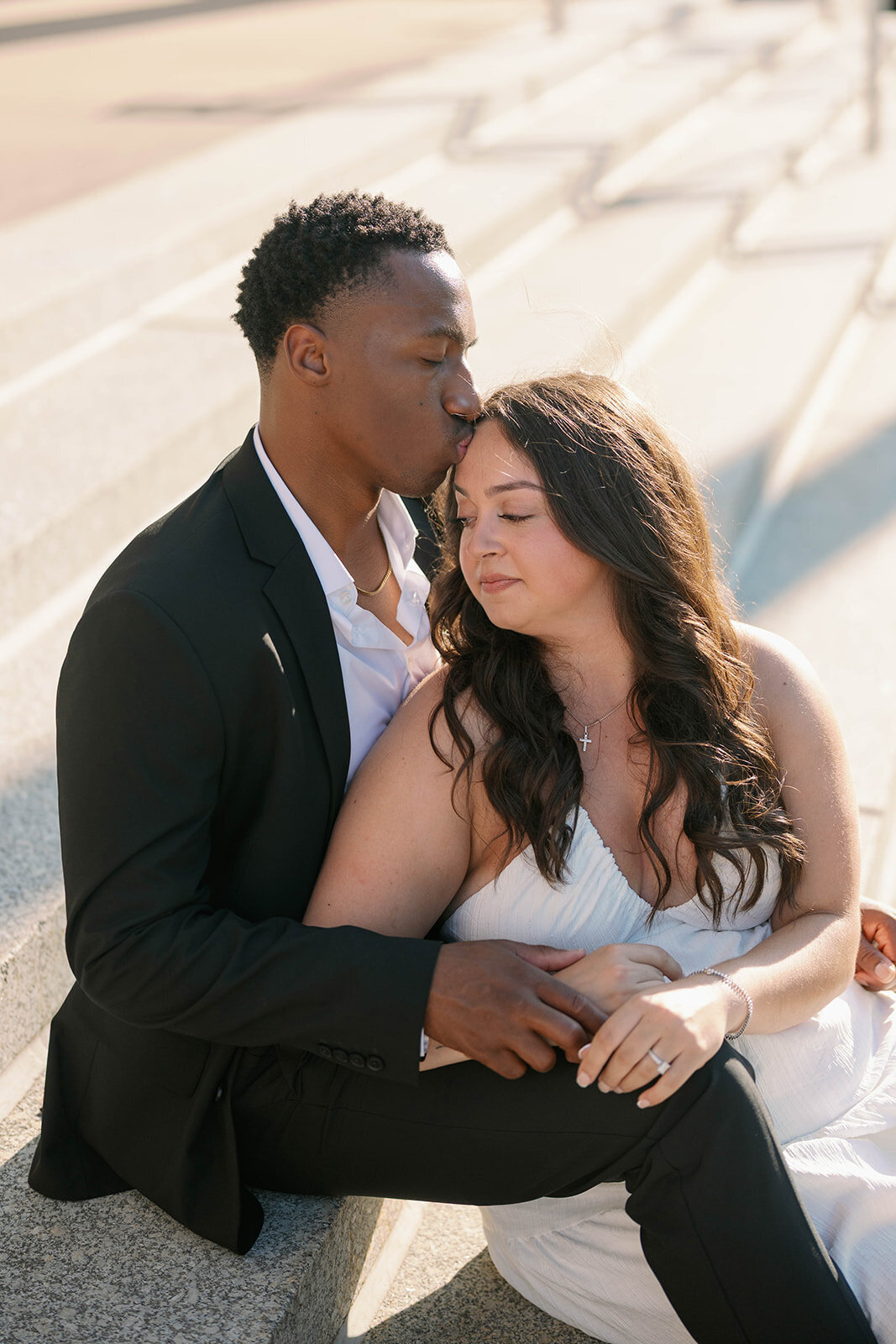 Groom-to-be kissing fiancée’s forehead during elegant downtown Kalamazoo engagement photoshoot.
