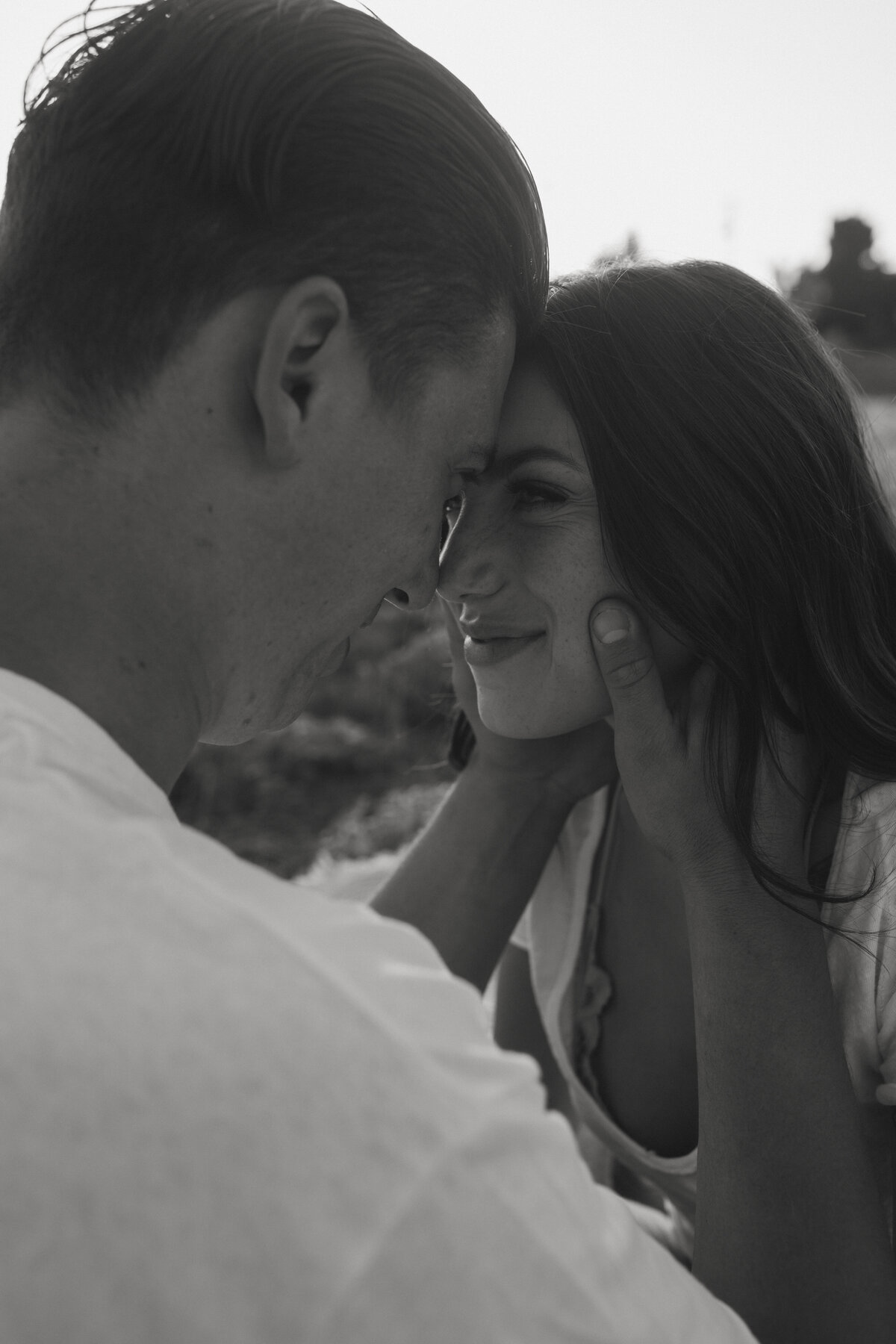 boyfriend embracing girlfriends face with hands looking into her eye in a field