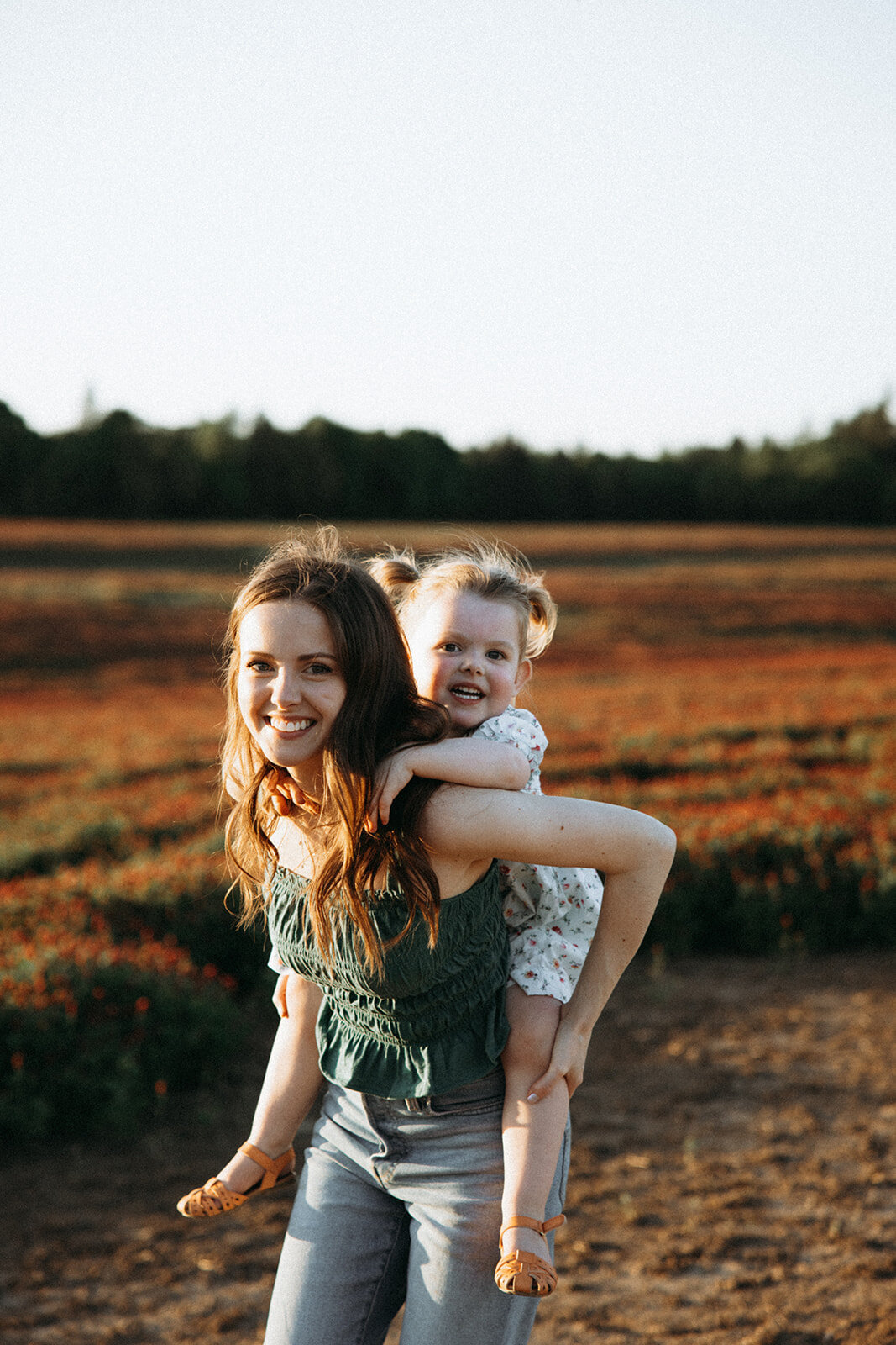 Mother gives her daughter a piggy back ride through red fields of clover in Oregon.