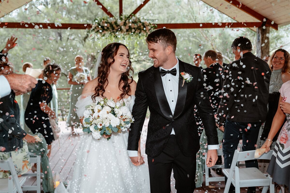 A newly married couple, beaming with joy and intertwined, gracefully exit the ceremony, their love captured in a candid moment.