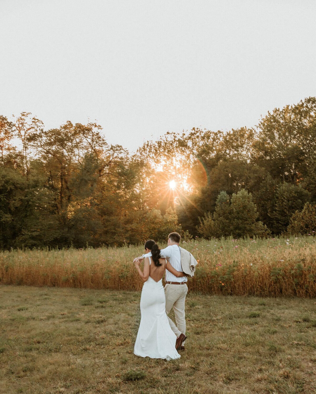 Bride and groom walking away together into a sunset-lit field