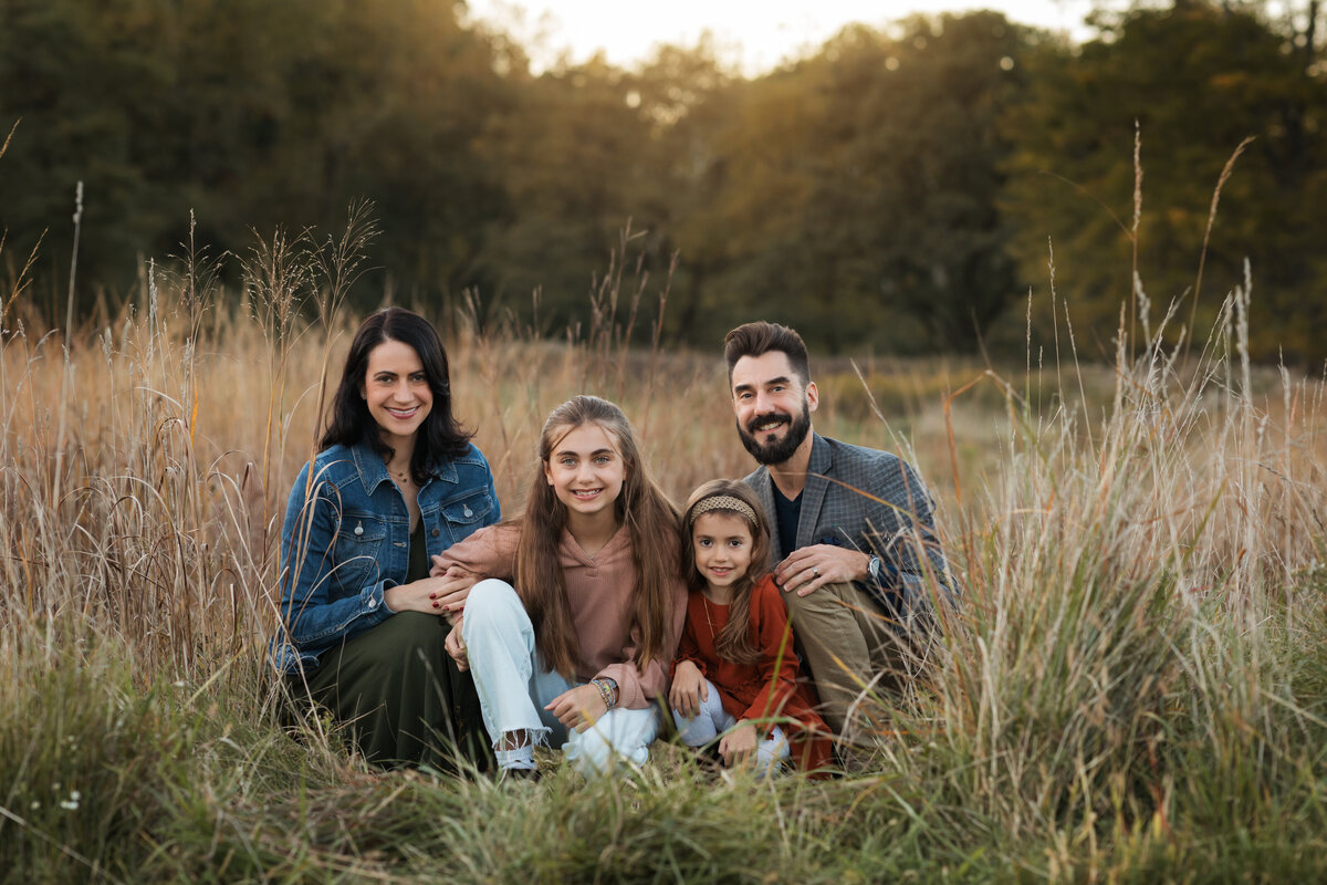 mom dad and two daughters posing in field for family photos 