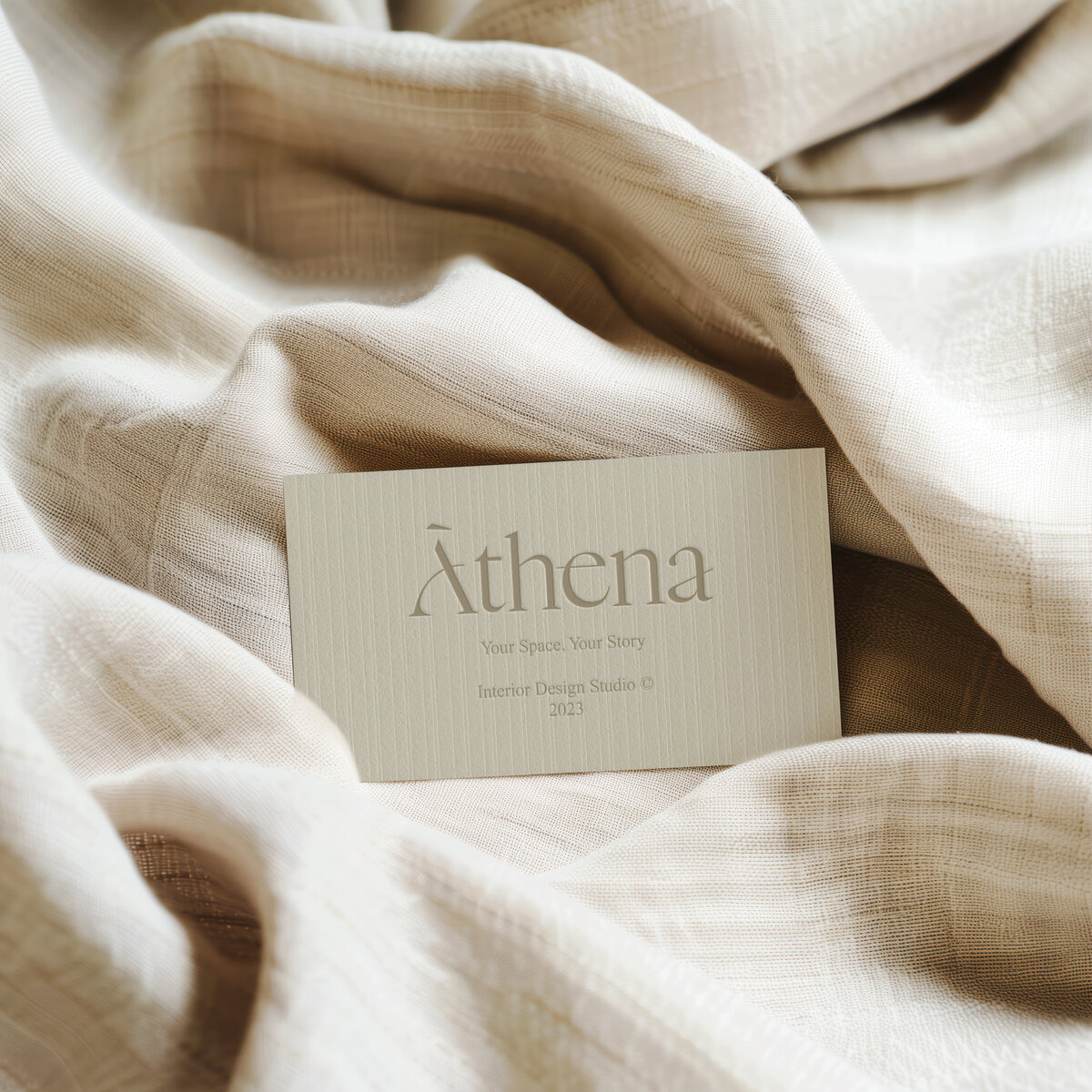 Athena brand identity with minimalist business card design for interior design studio, styled on neutral textured fabric.