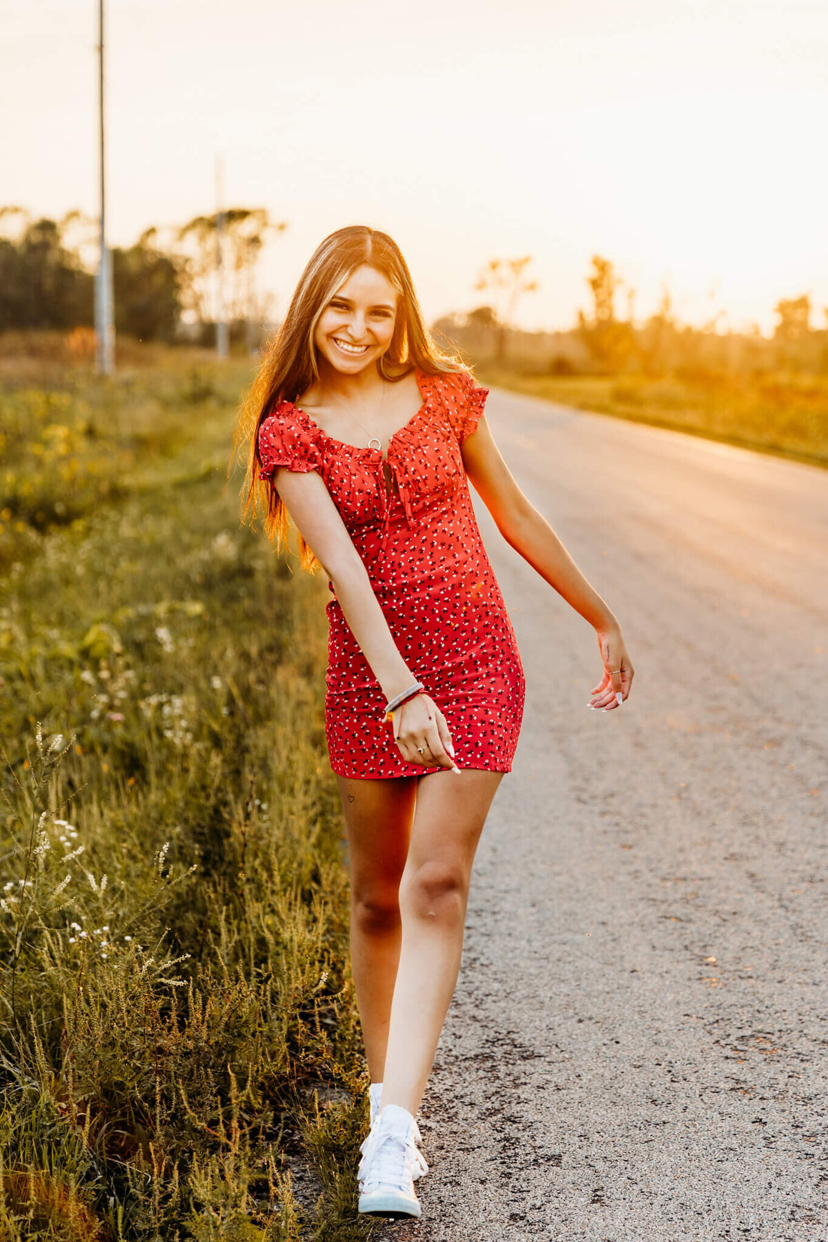 teenager in red dress walking a back road for senior photo session
