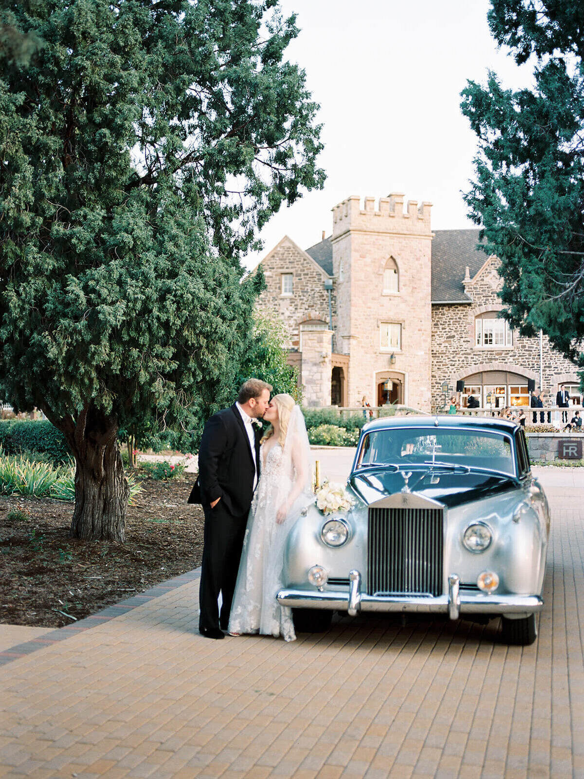 Bride and groom share a kiss by a classic car in front of a castle in Colorado