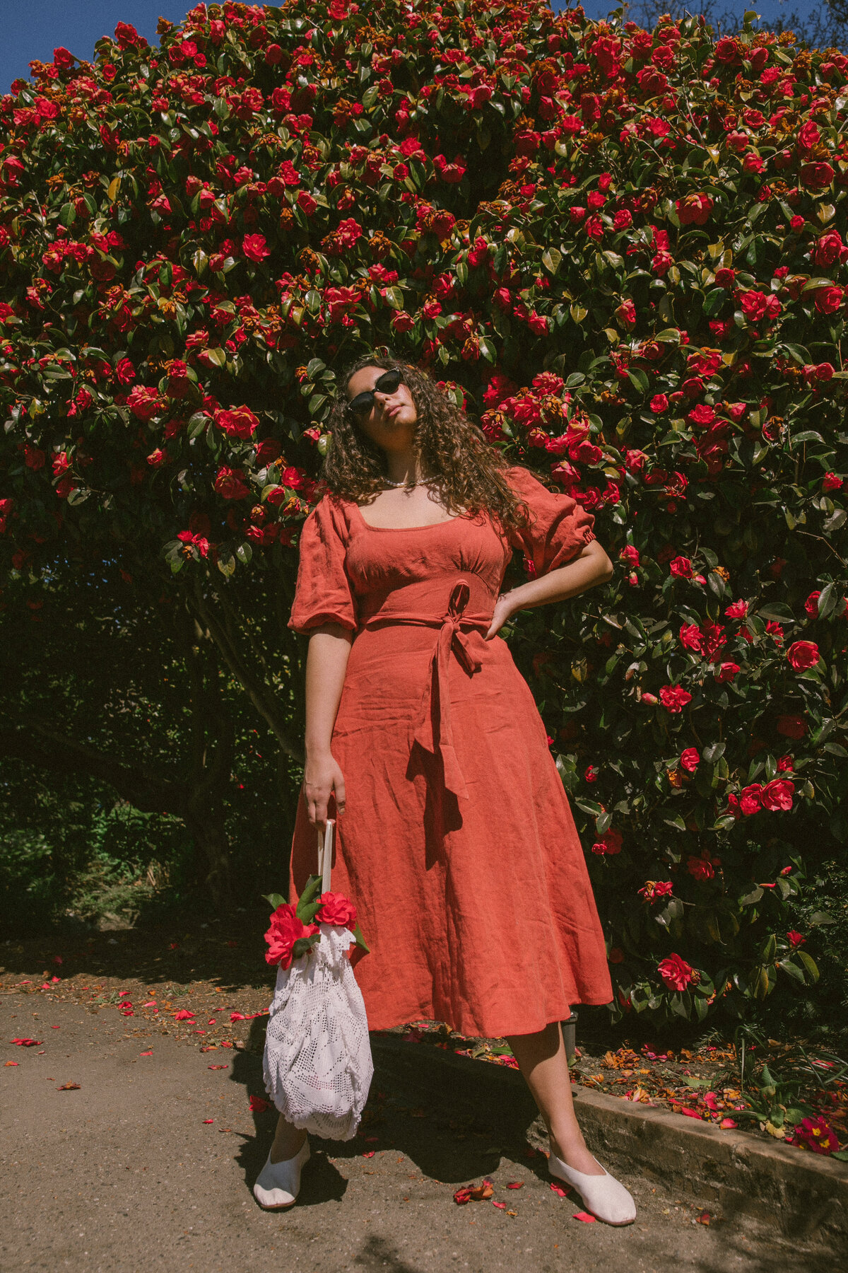 Picture of model in red linen dress and red flower bush