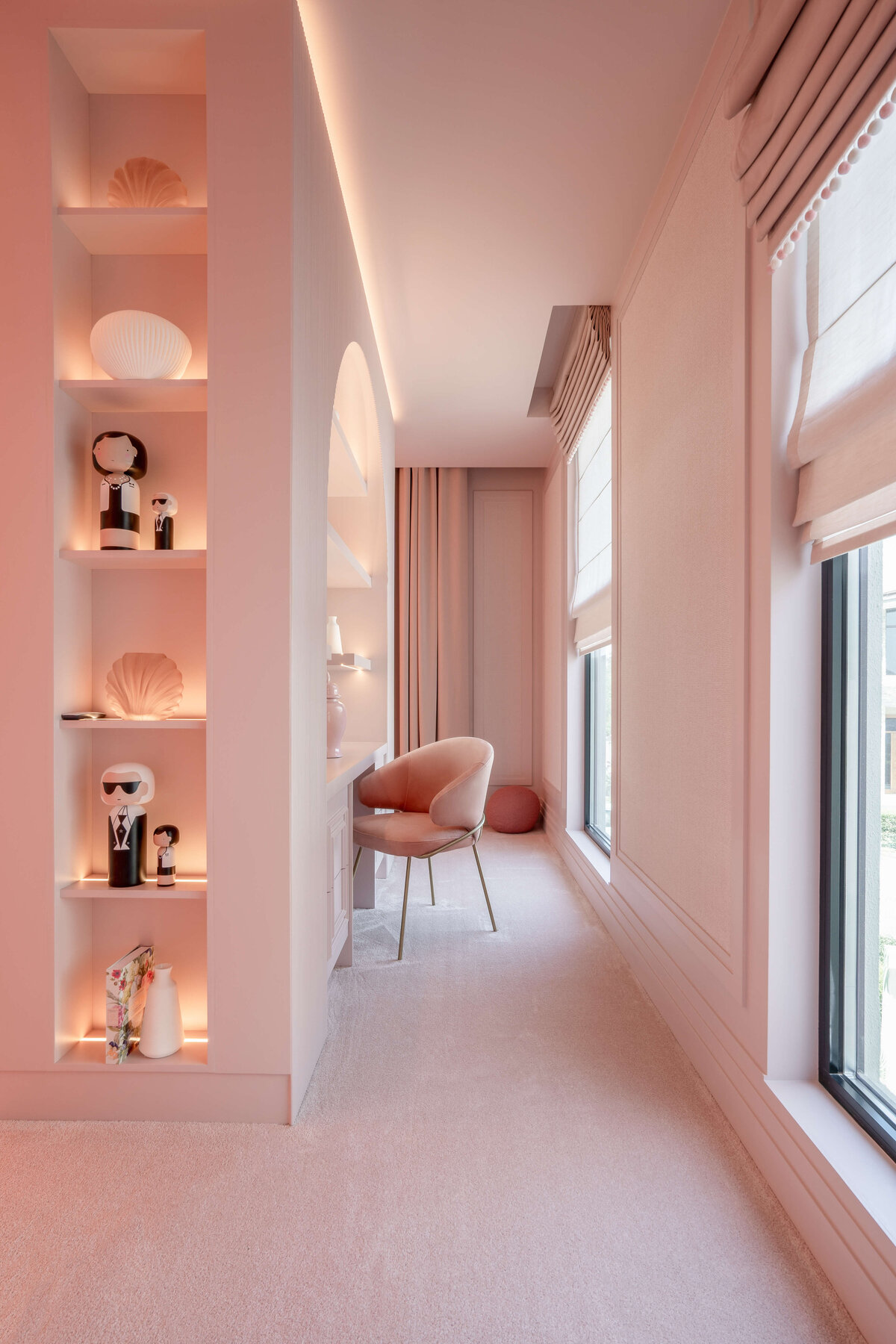 An alcove in a girl's pink bedroom. The alcove leads to a built-in desk with a pink chair. Across from the desk are large windows.