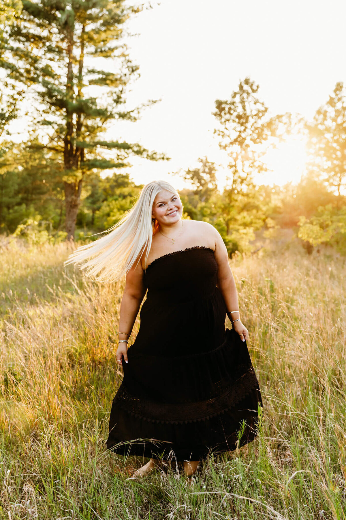 stunning high school girl in a black dress twirling in a grassy field at sunset
