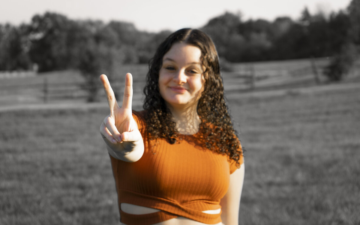 Senior portrait of a girl in an orange shirt holding up two fingers