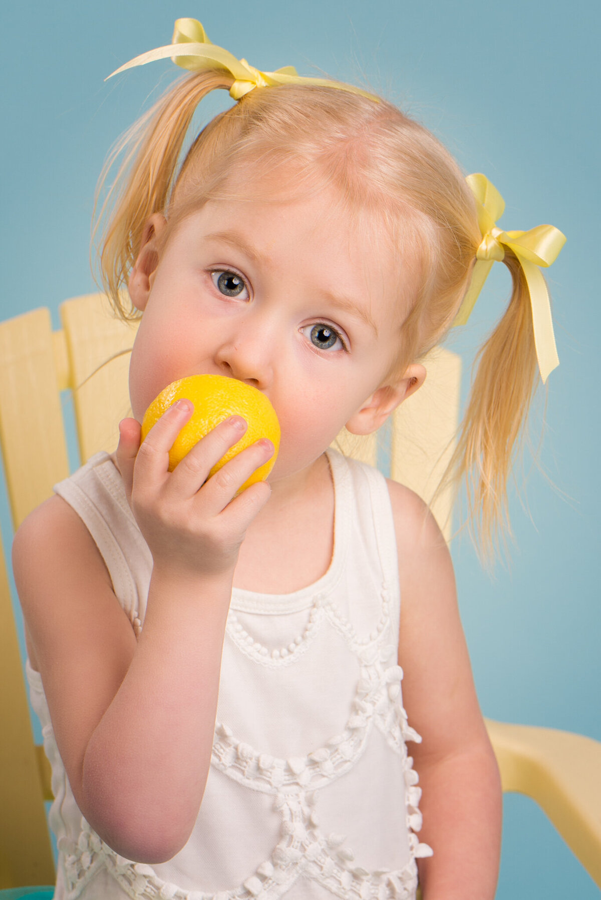 Playful portrait of a toddler enjoying a lemon against a light background, captured in Overland Park, Kansas. Perfect for families seeking candid and fun child photography in the Kansas City area.