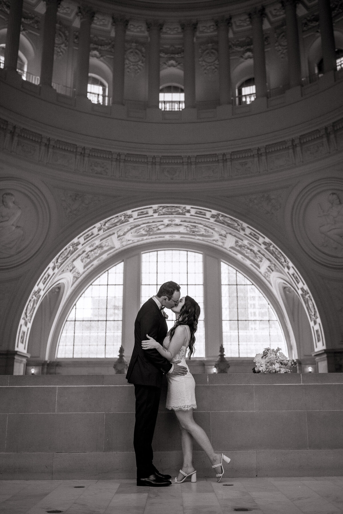 Wedding couple kissing at San Francisco City Hall after their elopement. They are framed in a semi circle window archway.