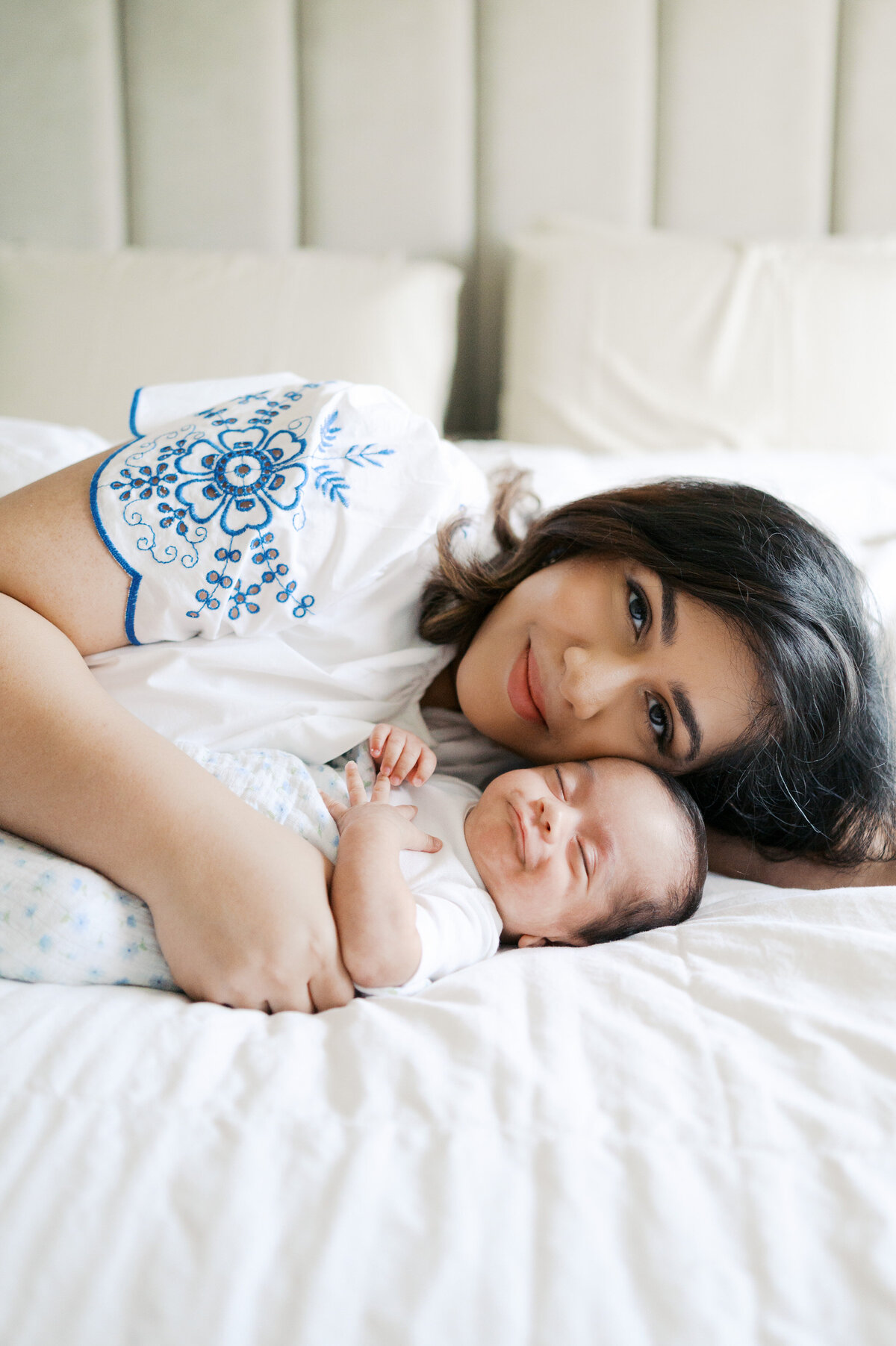 mom snuggles with newborn baby boy while he smiles