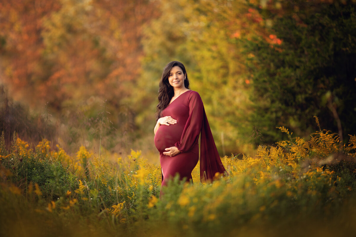 A pregnant mother stands in a field of wildflowers holding her bump at sunset