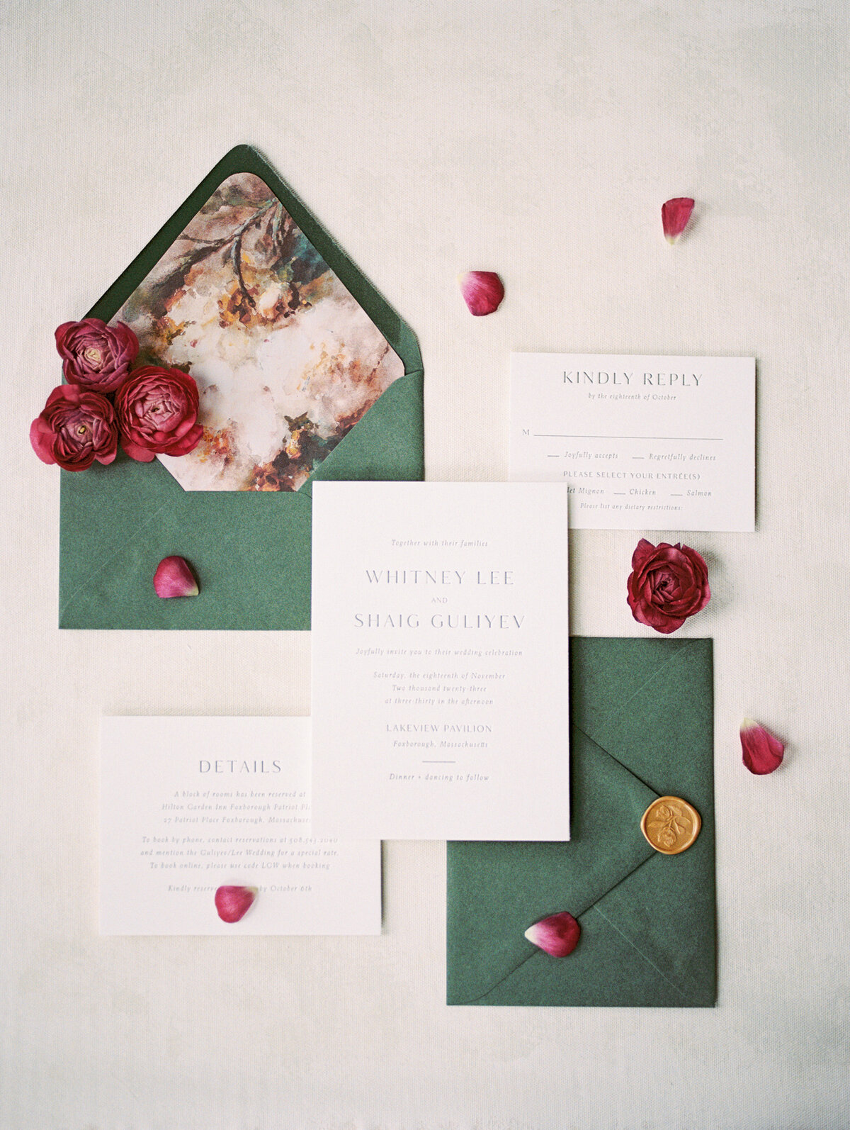 Flat lay of a dark green and white weddding invitation suite with dark pink flowers