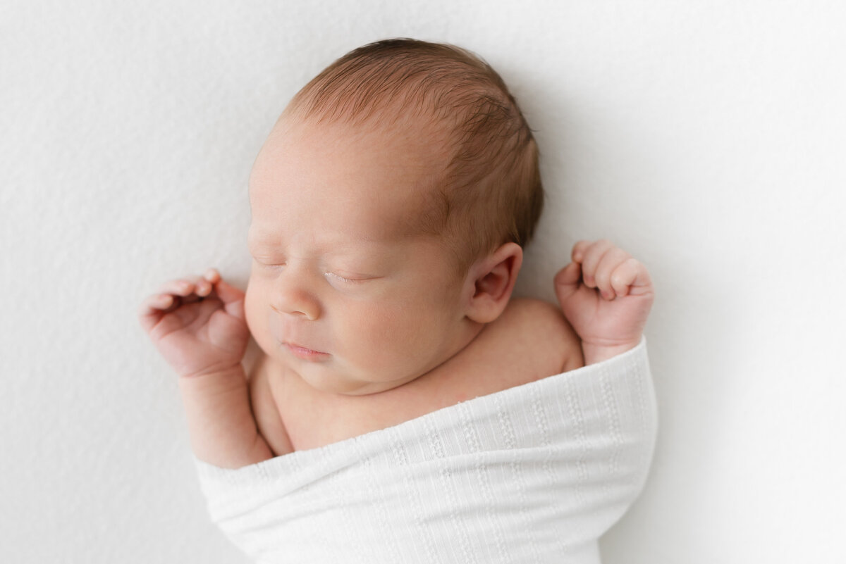 A waist up photo of a baby boy swaddled laying on a white blanket by Washington DC Family Photographer