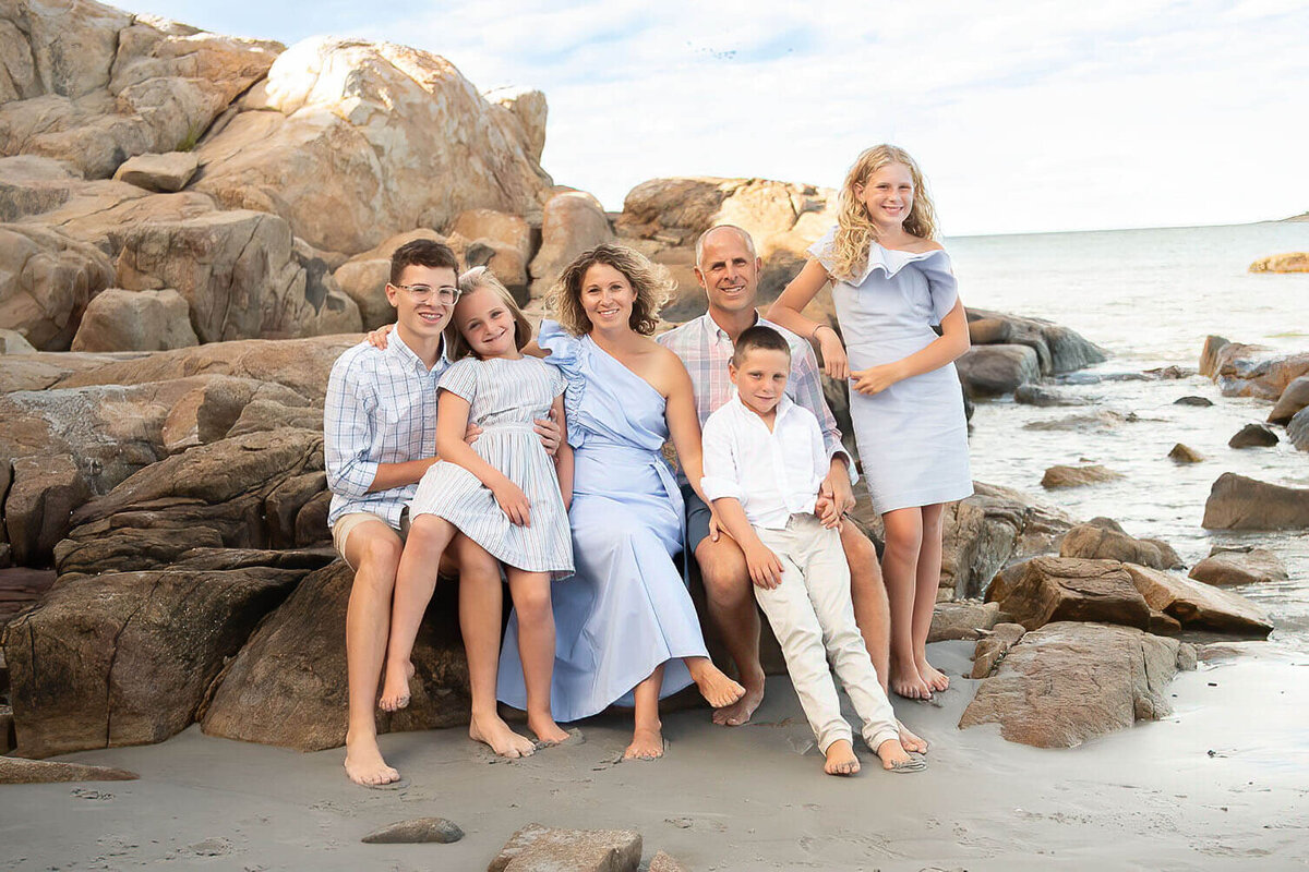A family of six dressed in white and blue pose on a rock at Wingaersheek Beach.