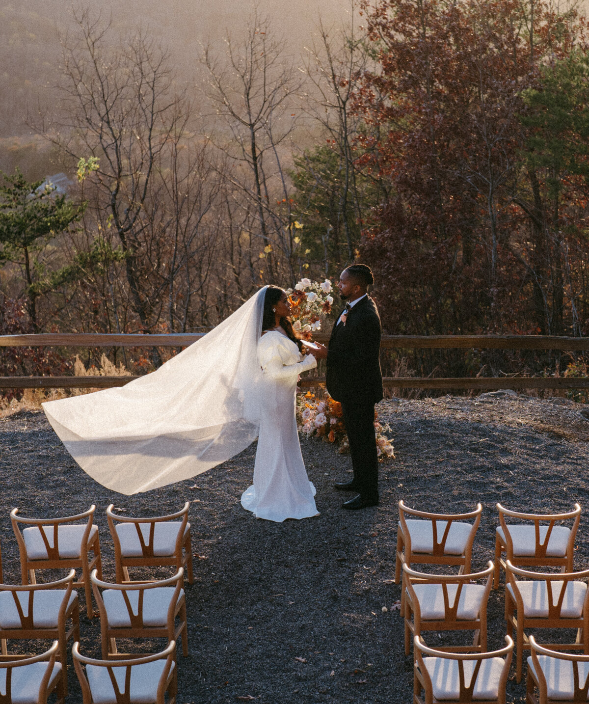 Bride and groom exchanging vows at mountaintop outdoor ceremony with flowing veil and autumn foliage
