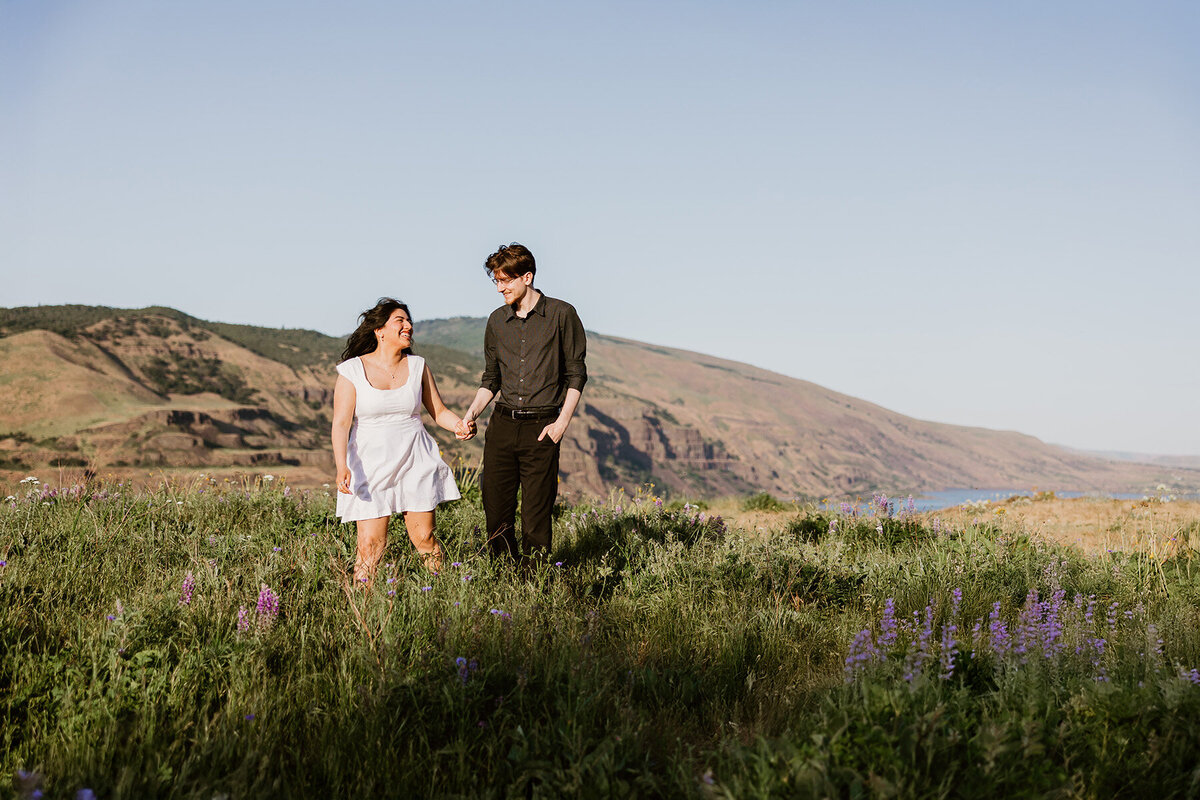A happy newly engaged couple dances through a field of flowers at sunset