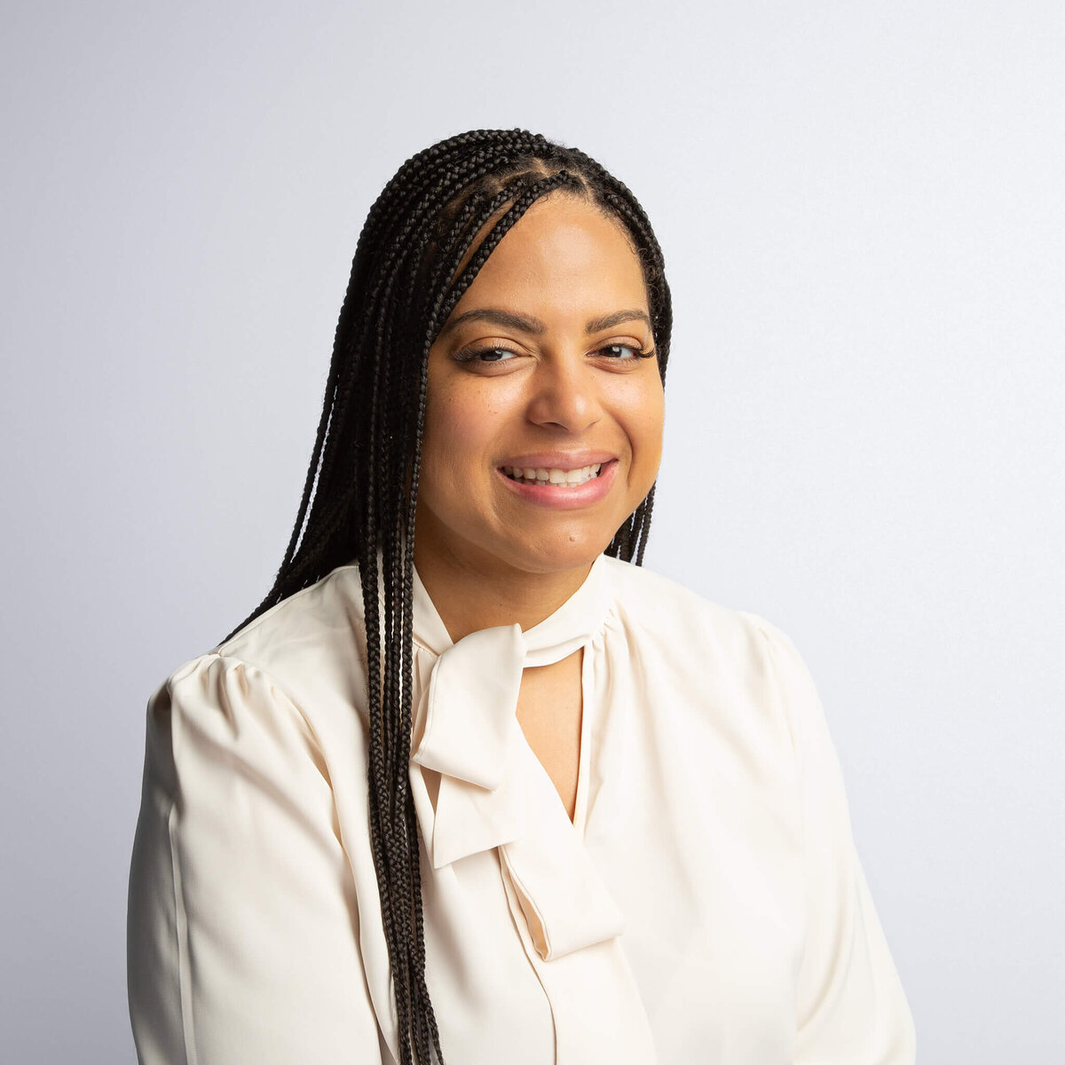 Headshot portrait of a woman with long black hair, wearing a light cream shirt, in front of a light grey background.