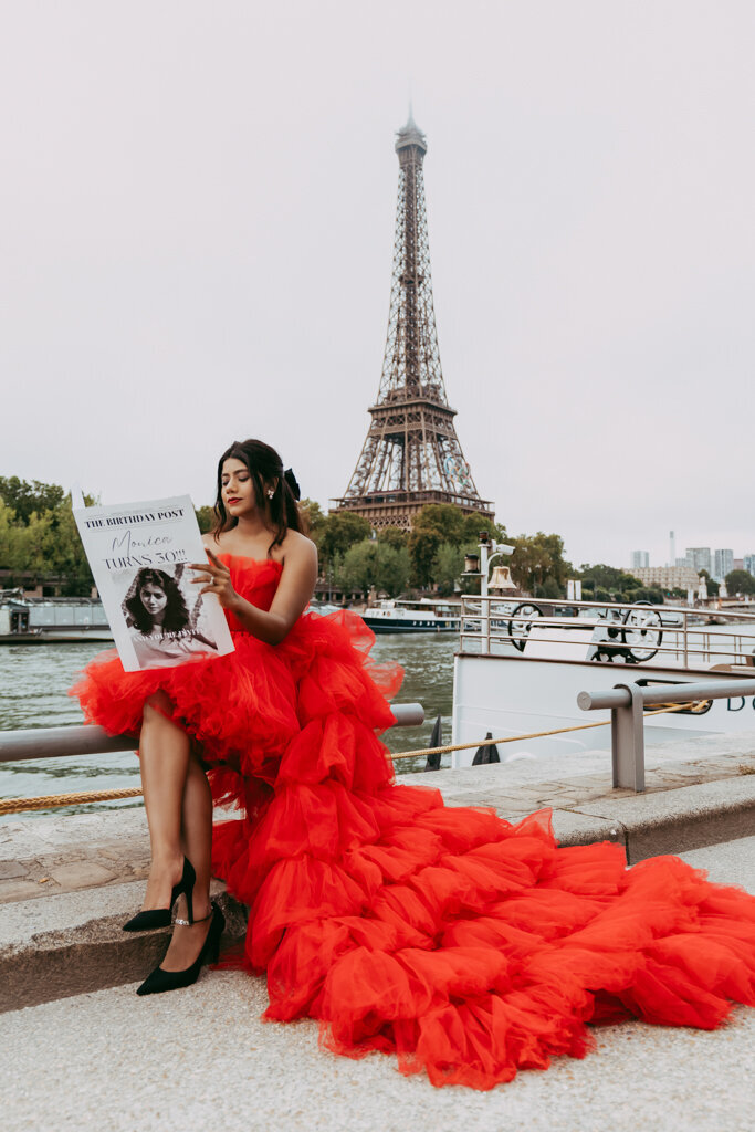 Lifestyle portrait by Seine river with woman in red dress reading newspaper overlooking Eiffel Tower