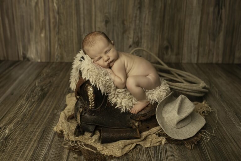 Newborn baby boy peacefully resting on a small saddle, nestled in soft fabrics, creating a charming and rustic western-themed portrait