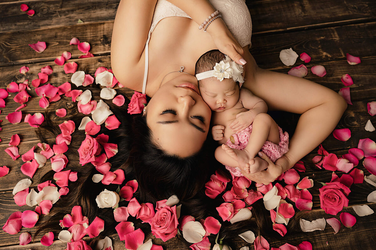 Mom laying down holding her baby girl surrounded by pink and white rose pedals at her Greater Toronto Newborn Photo shoot by Tamara Danielle.