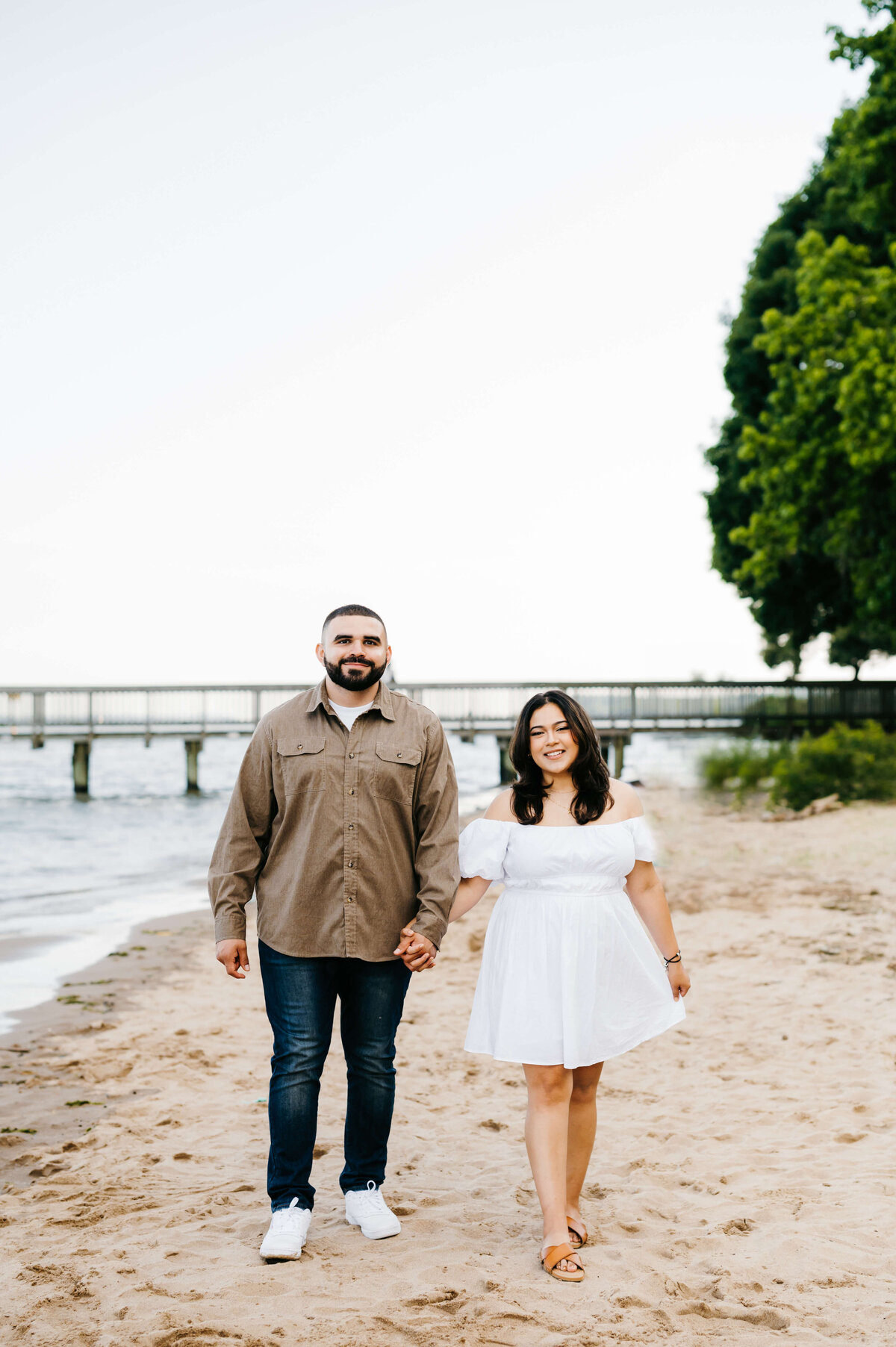 couples photography with man and woman on a beach holding hands and smiling for an engagement portrait