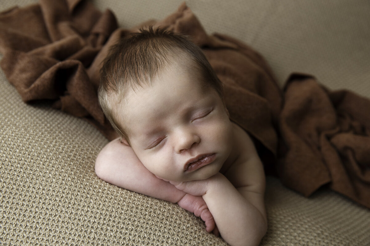 Portrait of a newborn baby with his chin on his hands  and laying on his tummy