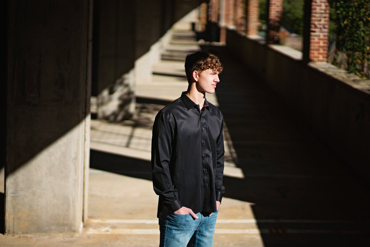A high school senior guy stands in a parking garage with dramatic lighting.
