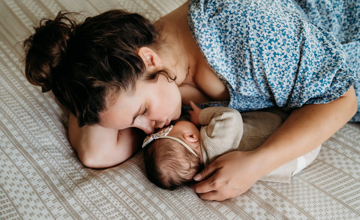 Newborn Photographer, A mother leans over her newborn baby and gives her a kiss on her head