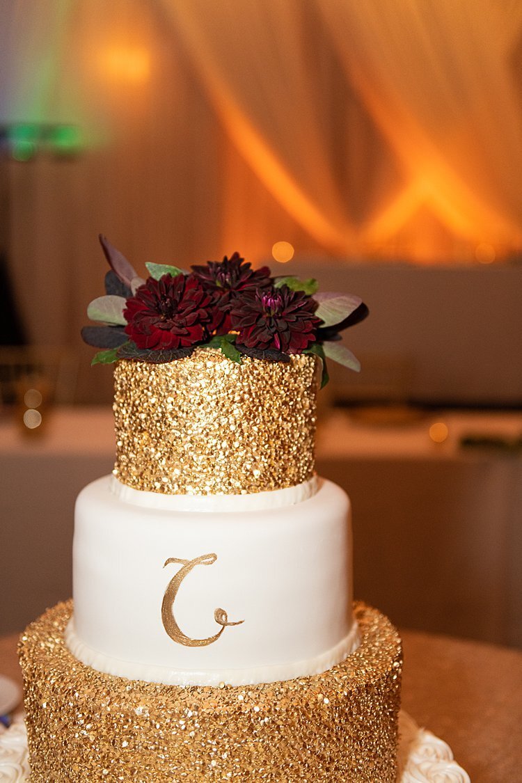Gold flecked wedding cake with monogram and red flowers